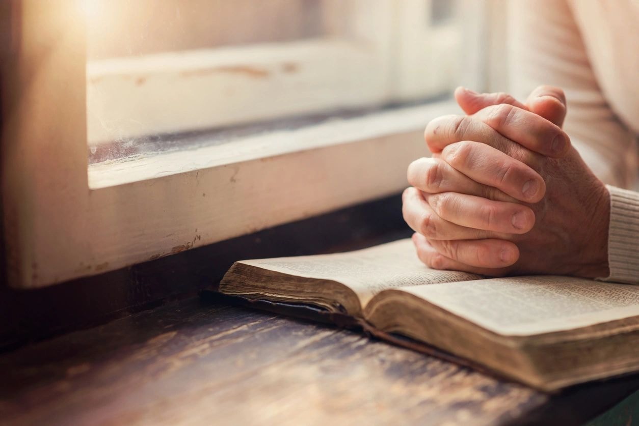 Hands clasped in prayer over Bible